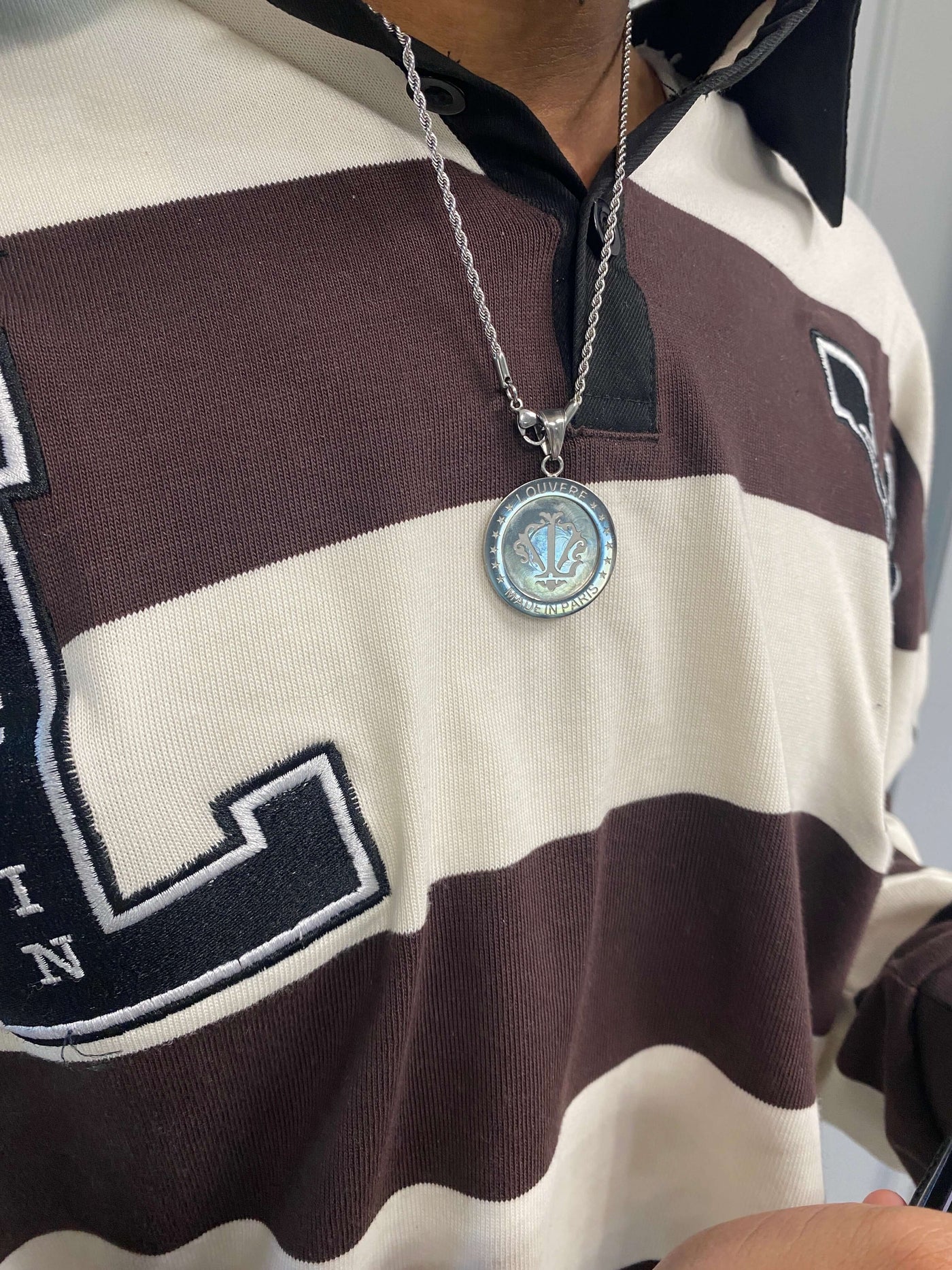 Close-up of a person wearing a striped polo shirt with a pendant necklace featuring a circular silver pendant.